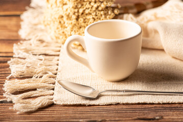 White cup, a beautiful white cup on a napkin and rustic wood surrounded by small flowers, selective focus.