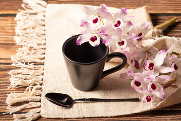 Black cup, a beautiful black cup on a napkin and rustic wood surrounded by orchids, selective focus.