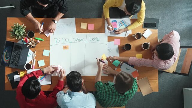 Top down aerial view of diverse business team making scrum task board at meeting room. Group of smart people writing at paper and sticky notes for making kanban board to manage work flow. Convocation.