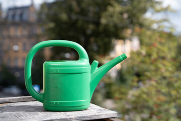 Green Plastic Watering Can on a Wooden Table Outdoors © Edgars