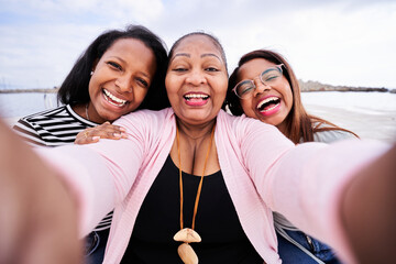 Mother and daughters enjoying a sunny day at the beach, smiling and taking a cheerful selfie together. Creating joyful memories and bonding in a beautiful outdoor setting