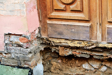 Deteriorated wall foundation with cracked brick plaster erosion and decayed material showing unsafe structural condition and urgent restoration requirement in old building at the entrance door