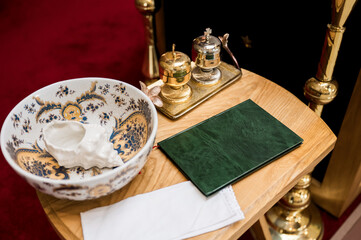 Religious ceremony items on wooden table with ornate bowl, shell, holy oils, green book, and cloth,...