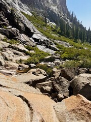 Jagged boulders and smooth granite slabs frame a tranquil mountain stream, with pine-covered slopes rising in the background