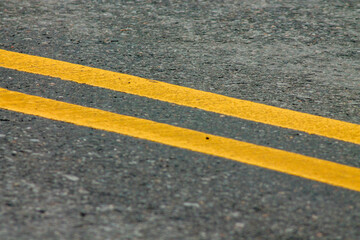 Fototapeta premium Yellow Lines on a Winding Road. Abstract turning road background with tires track and yellow striped road marking on dark asphalt. 
