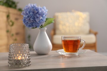 Vase with beautiful flower, tea and burning candle on table in room