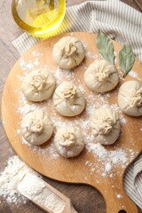 Uncooked khinkalis (dumplings) with flour, oil and bay leaves on wooden table, top view