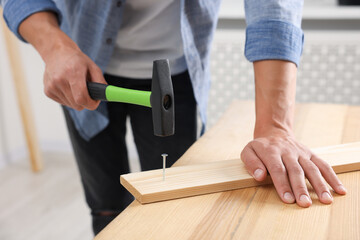 Man hammering nail into wooden plank indoors, closeup
