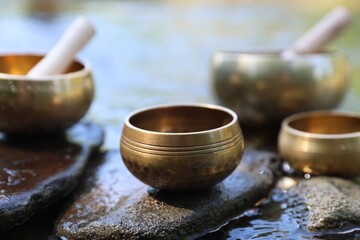Tibetan singing bowls with mallets on stones in river, closeup