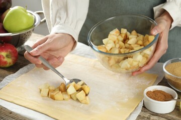 Making delicious apple strudel. Woman putting pieces of fruit onto dough at wooden table in kitchen, closeup