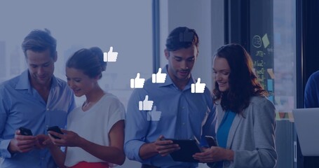 Standing business professionals using smartphones and tablet in office with thumbs-up icons