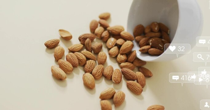 Spilling almonds from tipped white ceramic cup across kitchen tabletop, with social media icons - Powered by Adobe