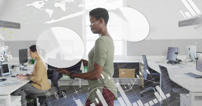 African American woman standing holding tablet in open-plan office, with laptop monitors and boxes - Powered by Adobe