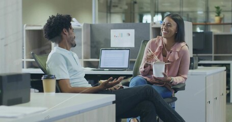 Gesturing male coworker leaning back and talking at open office desk, with chopsticks and laptop