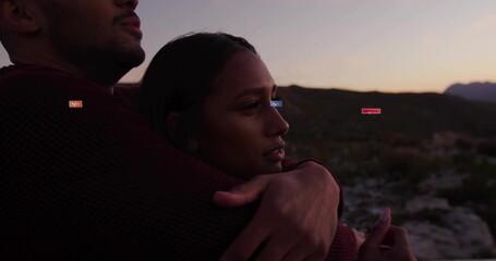 Embracing couple overlooking rocky valley at dusk, with burgundy knit sweater and brownish knit top