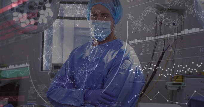 Standing surgeon wearing blue gown crossing arms in operating room, with monitor, data overlay