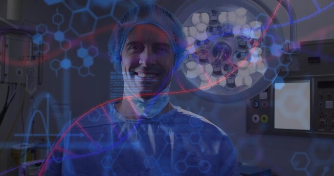 Smiling surgeon wearing scrubs under surgical light in surgery room with monitors and red DNA helix