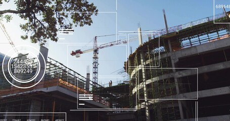 Standing construction workers wearing helmets vests on scaffolding at job site, with tower crane