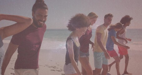 Group of six friends walking barefoot along ocean edge amid gentle waves, wearing summer attire