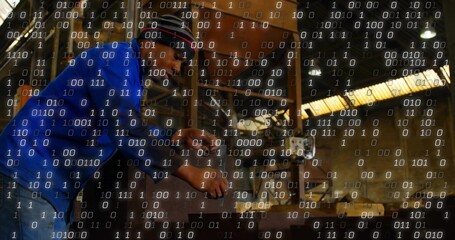 Operating machinist wearing ear protection adjusting lathe controls in workshop, binary overlay