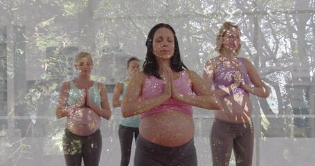 Four pregnant women wearing sportswear holding prayer pose in yoga studio, with yoga mats