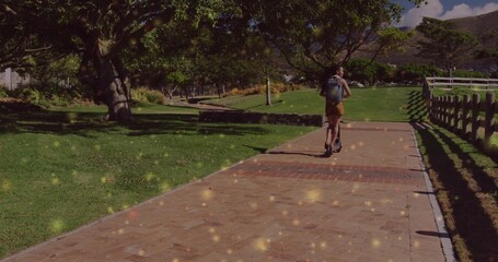 Riding woman wearing summer clothes on kick scooter along brick path in park, copy space