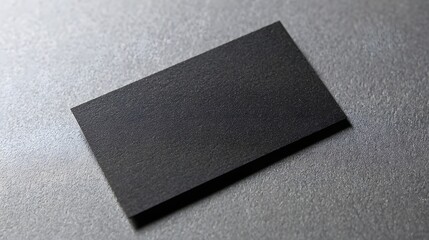 A close-up view of a dark gray business card lying on a textured gray surface.