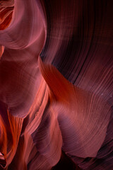 Obraz premium Flowing sandstone walls of Antelope Canyon in Arizona illuminated by desert light, revealing red, orange, and purple hues that highlight the canyon’s smooth textures and abstract geological beauty