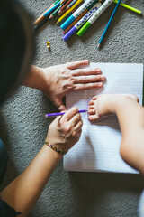 Parent tracing baby’s foot on notebook with colored pencils