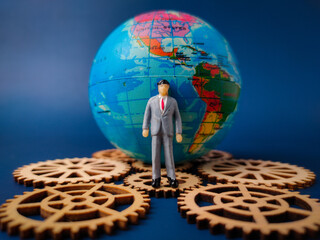 The image depicts a miniature businessman figure standing in front of a globe, with several wooden...