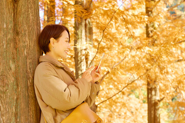 紅葉の中でスマホを使う女性　ミドルエイジ