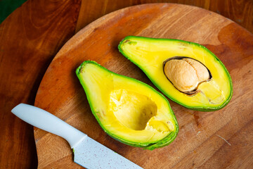 Close-up of a ripe avocado cut in half with a seed and creamy yellow flesh on a wooden cutting...