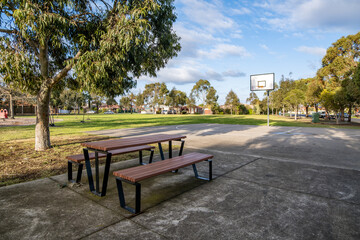 Public park with picnic tables, benches, and a basketball hoop in a suburban neighborhood of Melbourne, Australia. Concept of outdoor recreation, community facilities, and family-friendly spaces.
