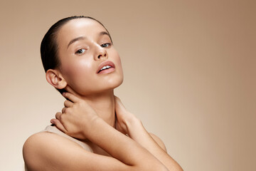 A young model with a natural complexion poses softly against a warm beige background, exuding...
