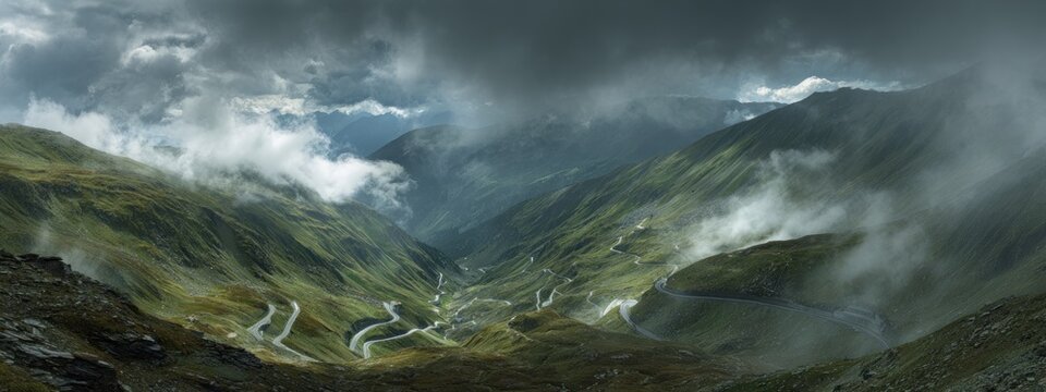 A winding mountain road cuts through a valley, enveloped by fog under a dramatic, overcast sky with green hills - Powered by Adobe