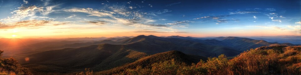 Panoramic vista of mountain peaks basked in golden hour light under a partly cloudy azure sky, with amber vegetation in the foreground