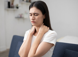 Young woman sitting on sofa and bed at home, muscle pain, body aches, back pain, massage, shoulder...