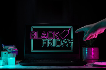 Hand pointing to a laptop with neon Black Friday sign, representing special discounts and...