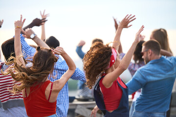 Group of diverse young adults dancing outdoors with arms raised, enjoying energetic movement...