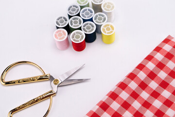 Sewing Still Life - Colorful Threads, Golden Scissors, and Red Gingham Fabric on White Background.