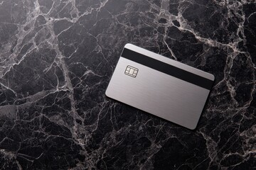 Silver credit card with chip and magnetic stripe on a dark marble background