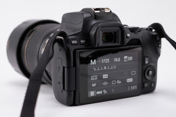 Black DSLR Camera with Lens and Strap on White Background, Display Showing Settings.