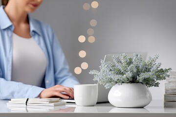 Woman working on laptop at a desk with decorative plants and a cup