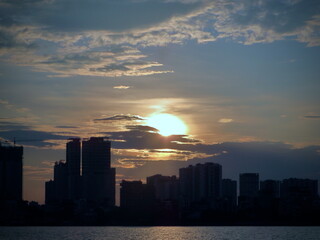 Cool Blue Dusk at West Lake, Hanoi – Sun Breaking Through Clouds over Modern Skyline