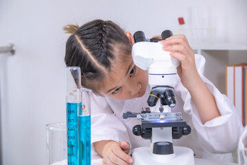 Young primary school student girl in white lab coat holding test tube with blue liquid, smiling and engaging in scientific activity, with laboratory equipment, educational science class back to school