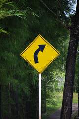 Bright Yellow Diamond Turn Ahead Warning Sign with Greenery
