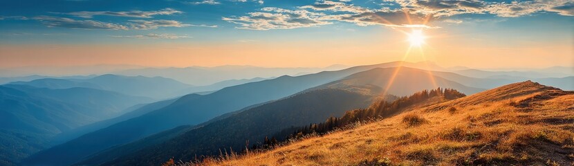 Obraz premium Scenic mountain range view at sunrise. Golden grass slope in foreground, blue hazy mountains, cloudscape, & bright sun