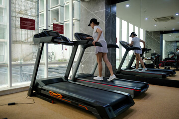 A woman wearing sportswear and a cap is using a treadmill in a gym