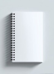 A blank, white spiral-bound notebook, casting a faint shadow, viewed from above on a pale surface