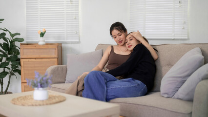 Asian adult lesbian couple cuddling embracing relaxing intimate bond cozy home living room sofa